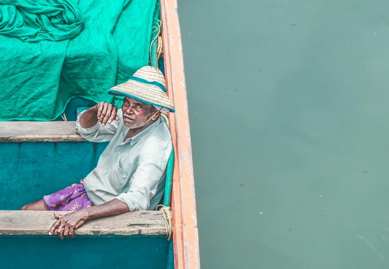 a man sitting in a boat on a body of water, pexels contest winner, mauve and cyan, vendors, fisherman's hat, indian master