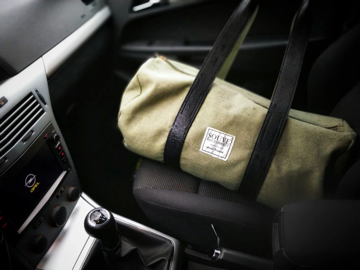 a duffel bag sitting in the driver's seat of a car, by Gen Paul, unsplash, bauhaus, olive green, promo image, rituals, (sfw) safe for work