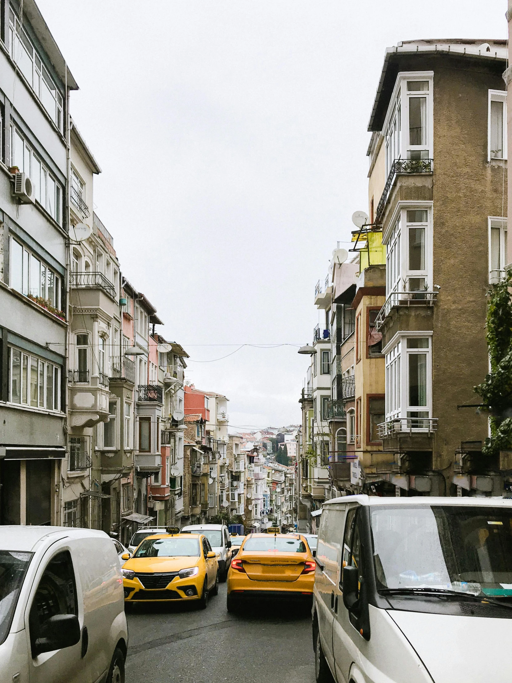 a street filled with lots of traffic next to tall buildings, a photo, inspired by Niyazi Selimoglu, yellow windows and details, built on a steep hill, 🚿🗝📝, promo image