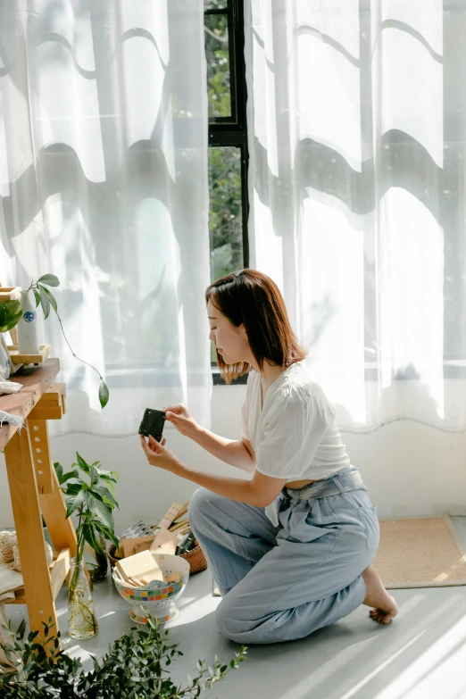 a woman sitting on the floor in front of a window, by Tan Ting-pho, home album pocket camera photo, holding gift, gardening, sun yunjoo