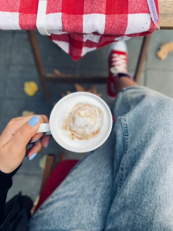 a person sitting at a table with a cup of coffee, whipped cream on top, sitting on the ground, promo image, multiple stories