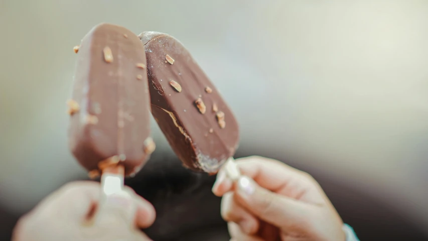 a close up of a person holding two ice lollies, fully chocolate, profile image