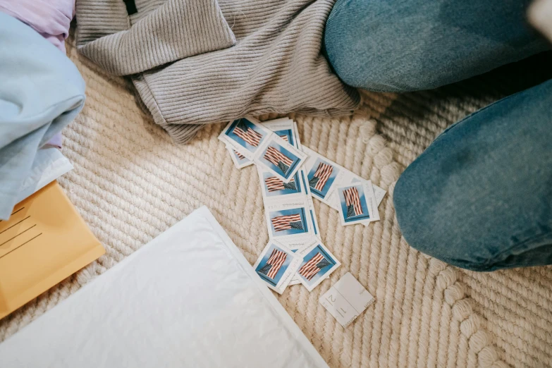 a woman sitting on the floor next to a pile of clothes, a polaroid photo, by Emma Andijewska, pexels contest winner, mail art, pair of keycards on table, game aesthetic, jeans and t shirt, tiny sticks