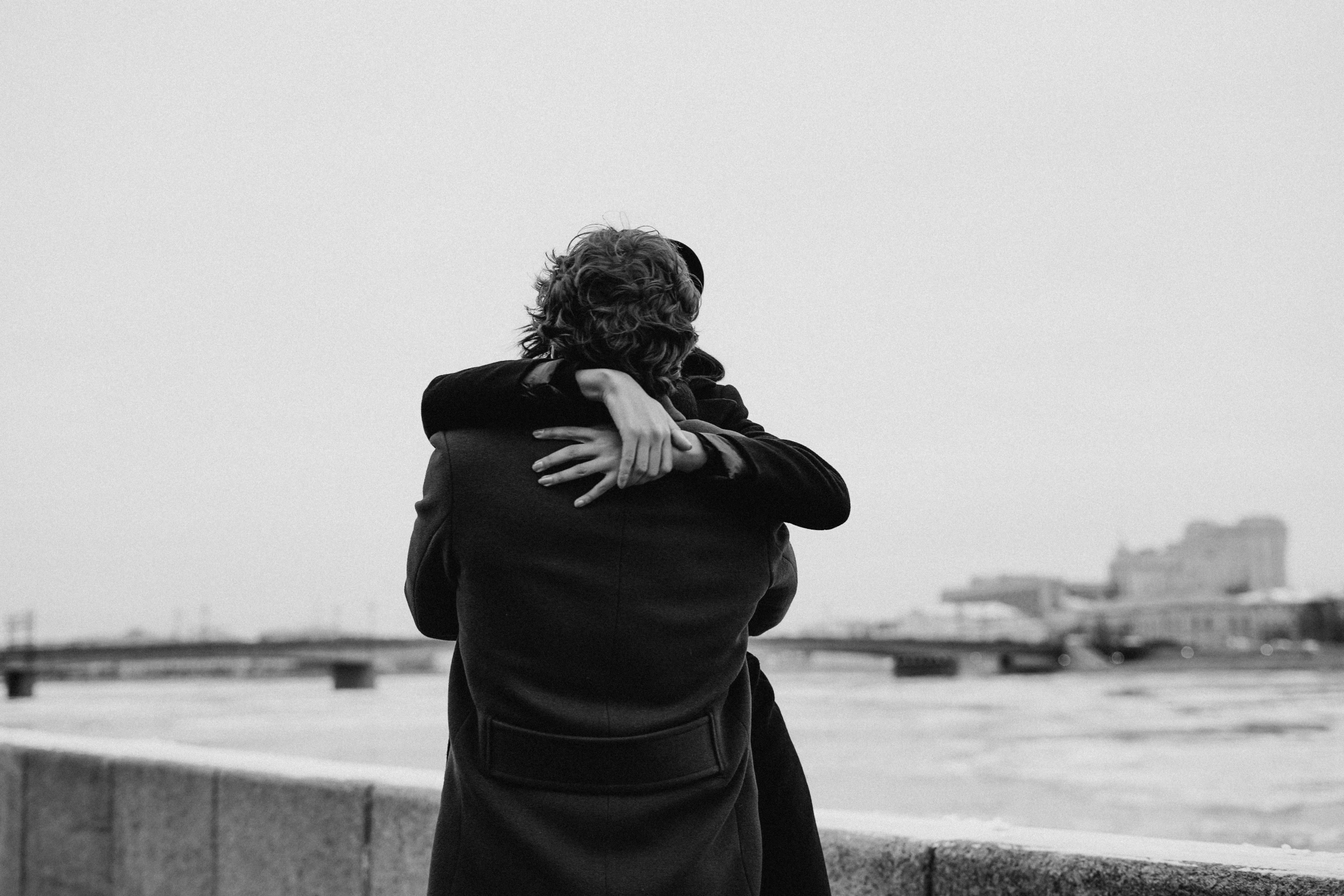 a black and white photo of a man hugging a woman, by Emma Andijewska, pexels contest winner, wearing black overcoat, overlooking, back, 15081959 21121991 01012000 4k