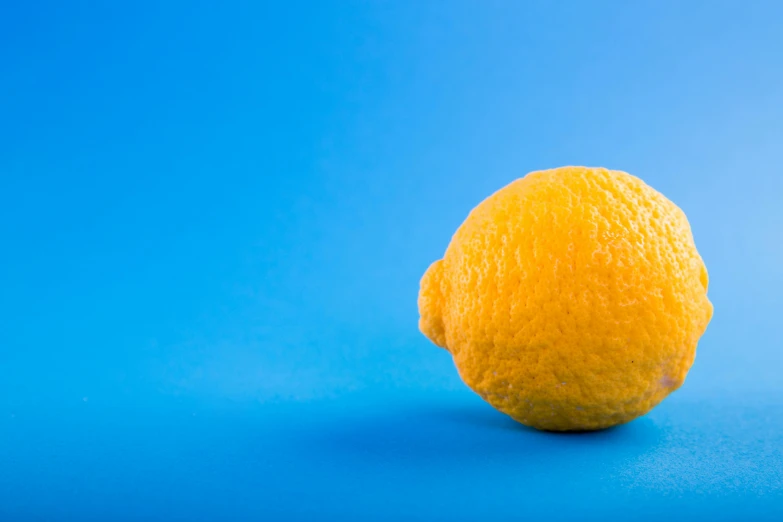 a lemon sitting on top of a blue surface, pexels, shot on sony a 7, with a bright yellow aureola, over-the-shoulder shot, wideangle