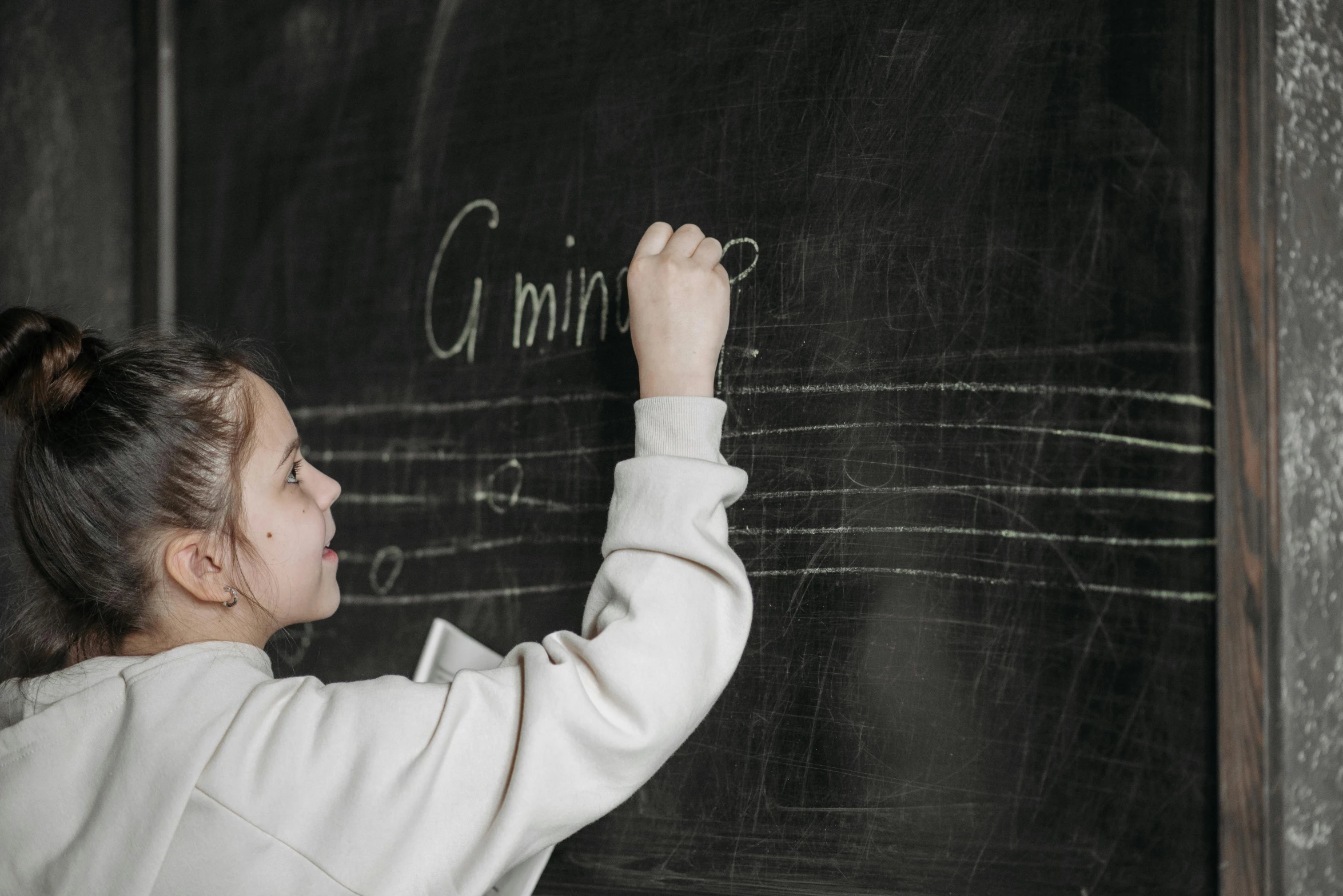 a little girl writing on a blackboard with chalk, by Emma Andijewska, pexels, side view of a gaunt, linear gamma, - g, background image