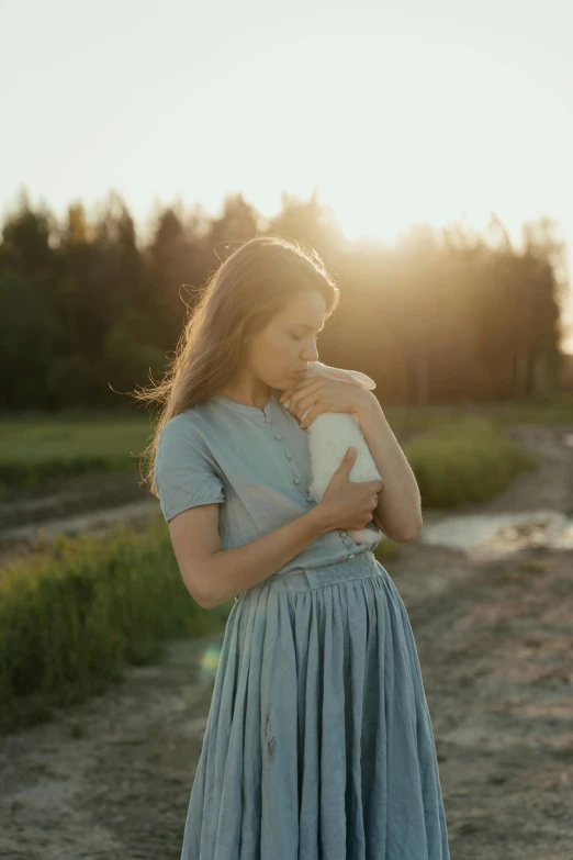 a woman in a blue dress standing on a dirt road, inspired by Anka Zhuravleva, unsplash contest winner, renaissance, holding a drink, young girl, in soft dreamy light at sunset, maternal