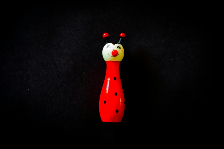 a toy in the shape of a ladybug on a black background, inspired by Kusama, unsplash, mingei, pestle, half wooden pinocchio, bowling, long boi