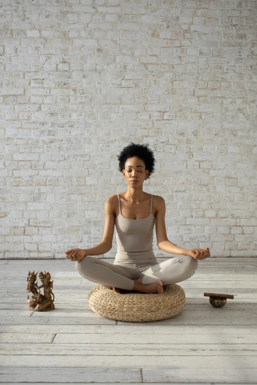 a woman sitting in a meditation position in front of a brick wall, curated collections, muted brown, natural materials, lotus pose