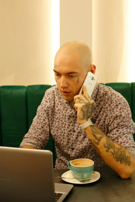 a man sitting at a table talking on a cell phone, brown buzzcut, with tattoos, laptop, damien tran