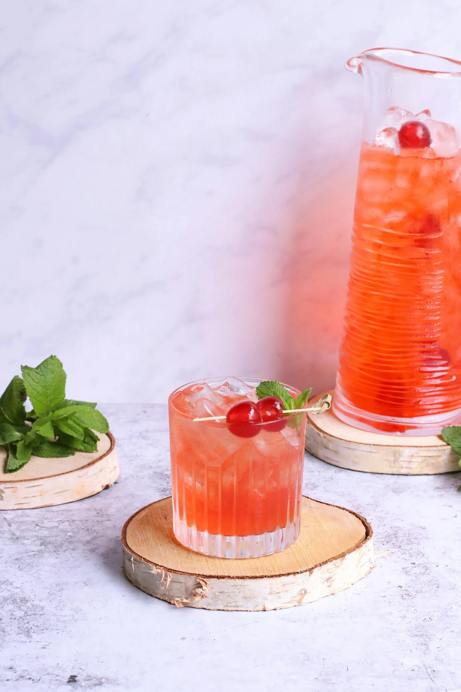 a pitcher of water sitting on top of a wooden coaster, inspired by Caesar van Everdingen, red blush, vodka, mint higlights, cherries