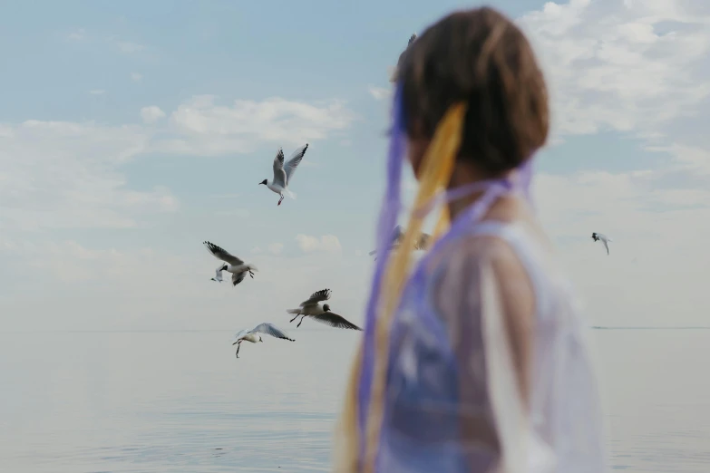 a woman looking at a flock of seagulls flying over the water, pexels contest winner, midsommar style, girl with feathers, photo of a ghostly pirate, connection rituals