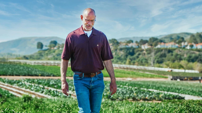 a man walking across a lush green field, a portrait, confident holding vegetables, profile image, jean luc picard, bay area