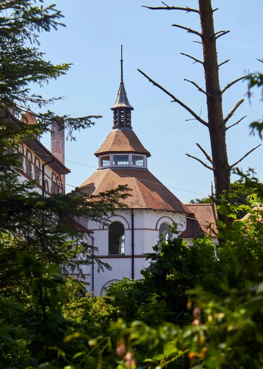 a church with a steeple surrounded by trees, inspired by Villard de Honnecourt, unsplash, quito school, rounded roof, color image, seaview, close-up shot taken from behind