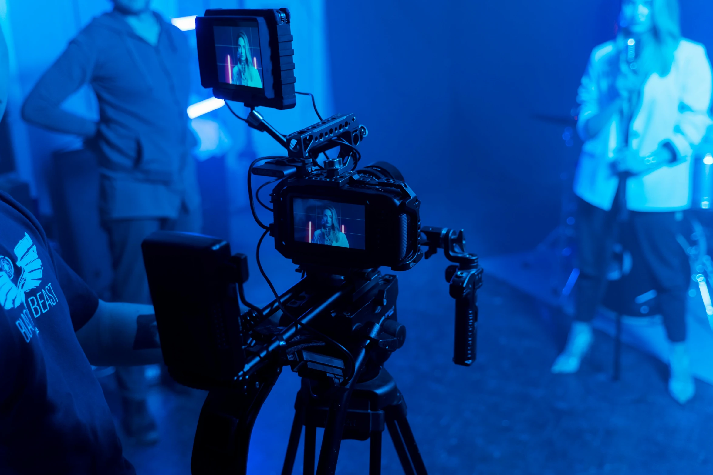a man standing next to a camera on a tripod, shutterstock, video art, cinematic blue lighting, movie set”, instagram post, live-action archival footage