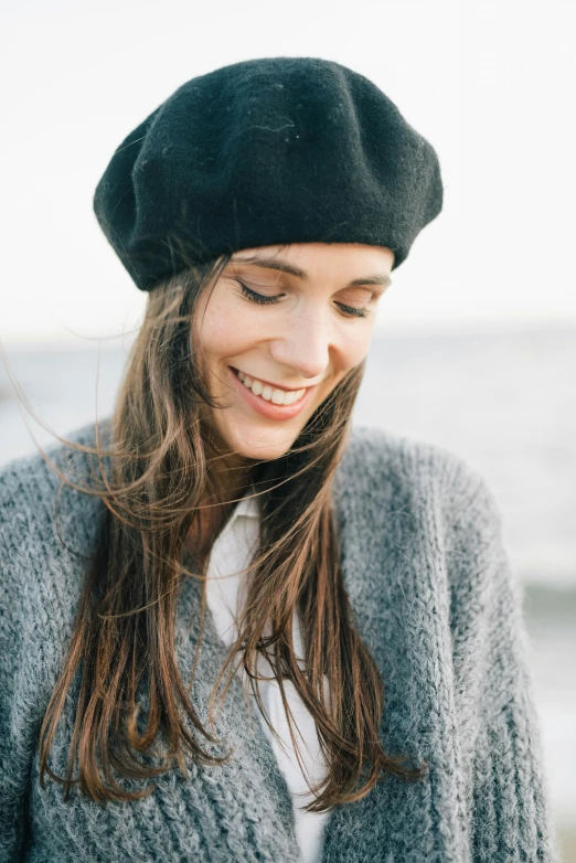 a woman standing on top of a beach next to the ocean, inspired by Anita Malfatti, trending on pexels, renaissance, black beanie, smiling softly, brunette, close up portrait of woman