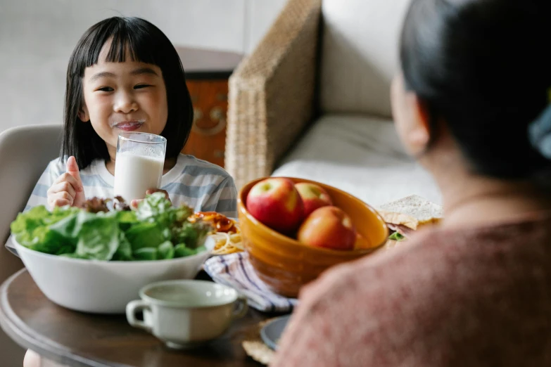 a little girl sitting at a table with a bowl of fruit and a glass of milk, pexels contest winner, an asian woman, family dinner, avatar image, ad image