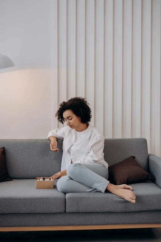 a woman sitting on a couch playing a game, pexels contest winner, minimalism, nathalie emmanuel, worried, holding gift, white l shaped couch