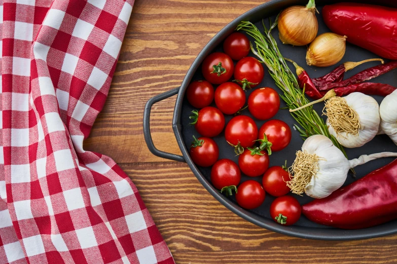 a pan filled with vegetables on top of a wooden table, by Julia Pishtar, tablecloth, red and black colour scheme, local foods, premium quality