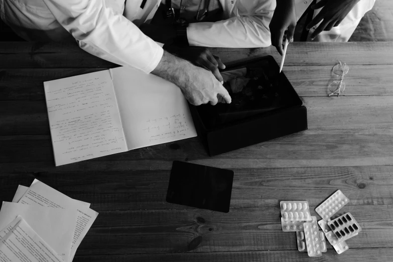 a group of people sitting around a wooden table, a black and white photo, pexels, process art, pills and medicine, holding notebook, wearing a labcoat, modern technology