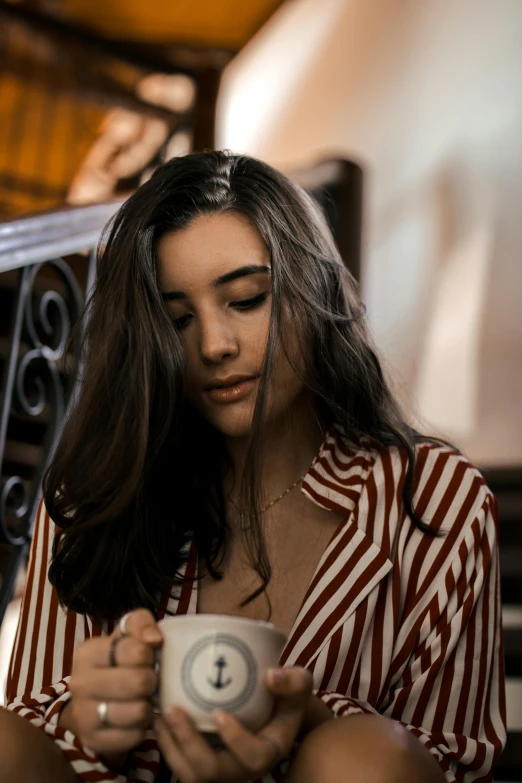 a woman sitting down holding a cup of coffee, inspired by Elsa Bleda, trending on pexels, renaissance, madison beer girl portrait, wearing stripe shirt, close up portrait photo, swirly dark hair