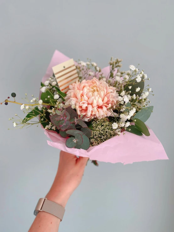 a person holding a bouquet of flowers in their hand, light pink mist, with lots of details, front and center, paper chrysanthemums