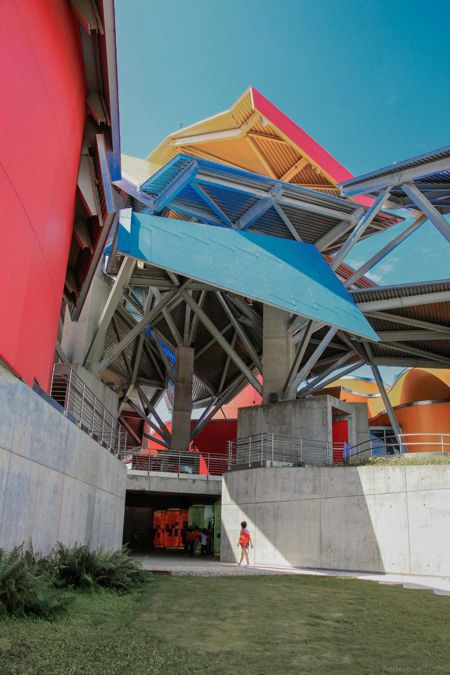 a man riding a skateboard on top of a lush green field, by Ned M. Seidler, conceptual art, red - yellow - blue building, frank gehry architecture, theater access corridor, canopies