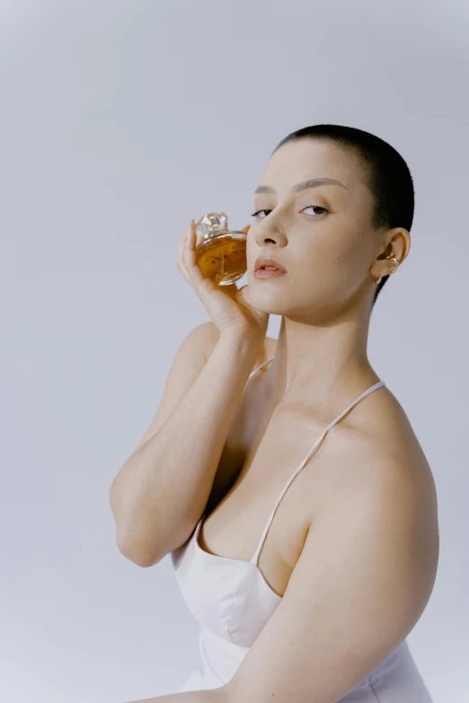 a woman in a white dress drinking from a glass, an album cover, unsplash, shaved head, portrait sophie mudd, perfume, wearing honey