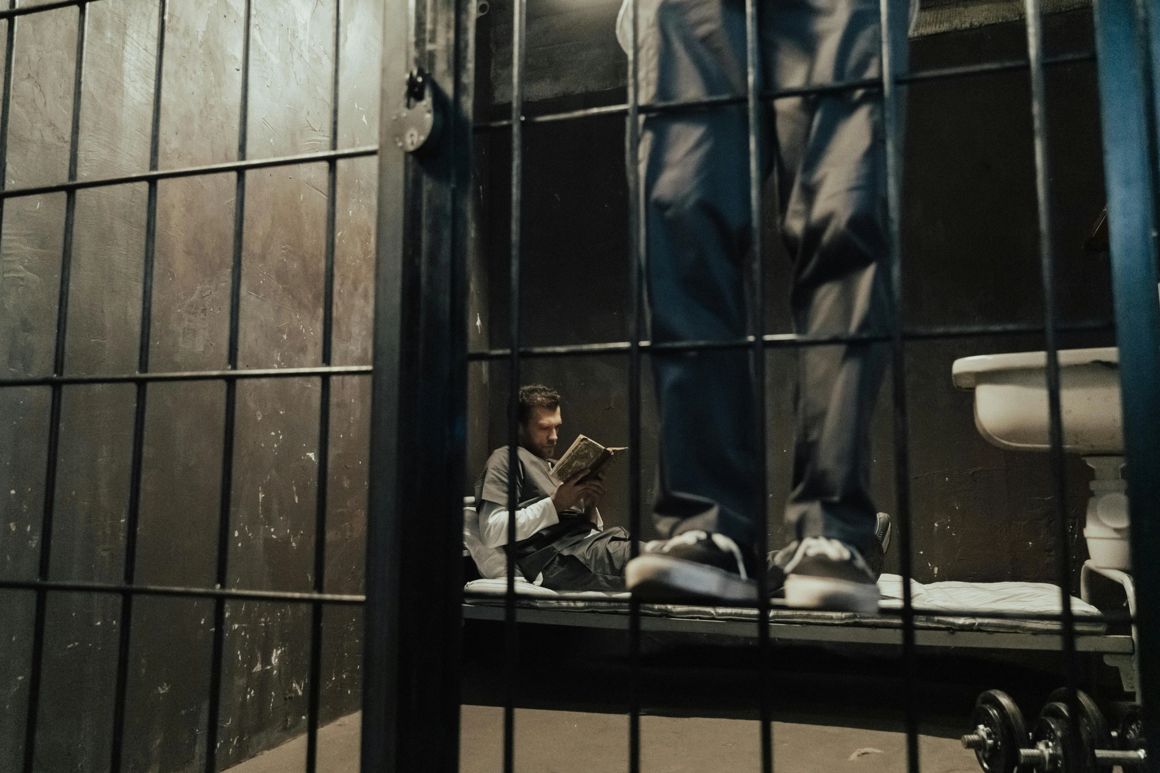 a man sitting in a jail cell next to a toilet, pexels contest winner, reading a book, cages, ( ( theatrical ) ), riyahd cassiem