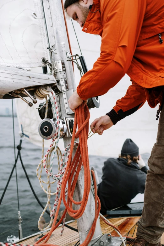 a man in an orange jacket working on a sailboat, pexels contest winner, hanging cables, grey, organic detail, adventure gear