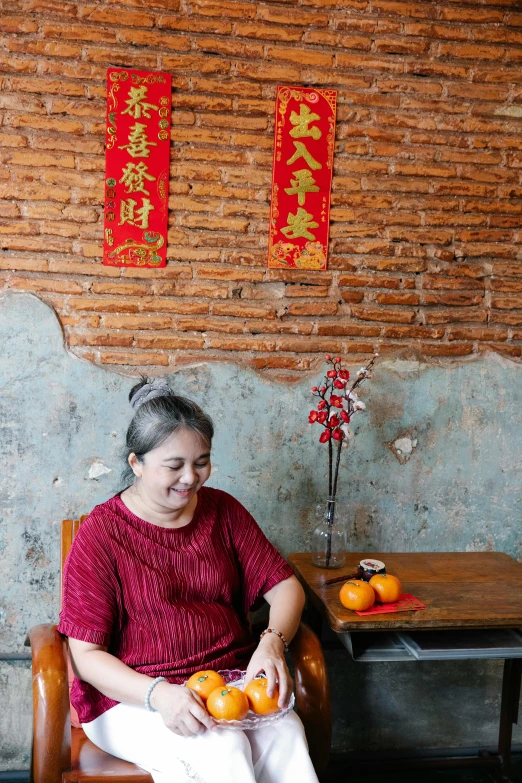 a woman sitting in a chair holding an orange, inspired by Cui Bai, happening, barong family member, sitting at the table, wearing a red cheongsam, jakarta