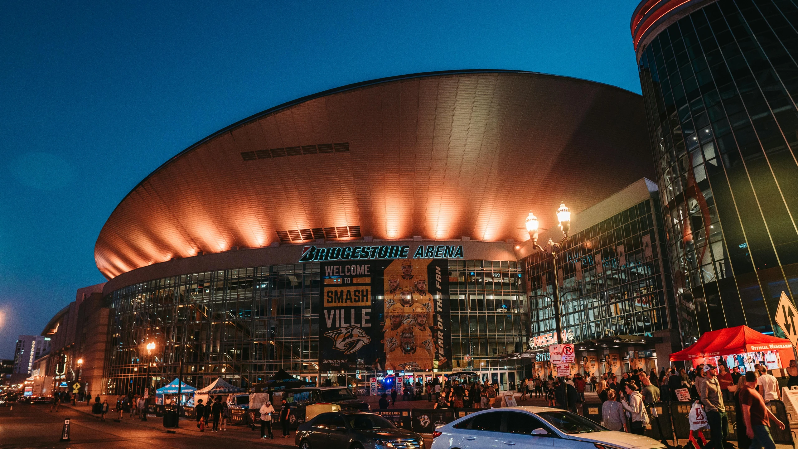 a group of people standing in front of a stadium, nhl, at night time, golden hour, tn