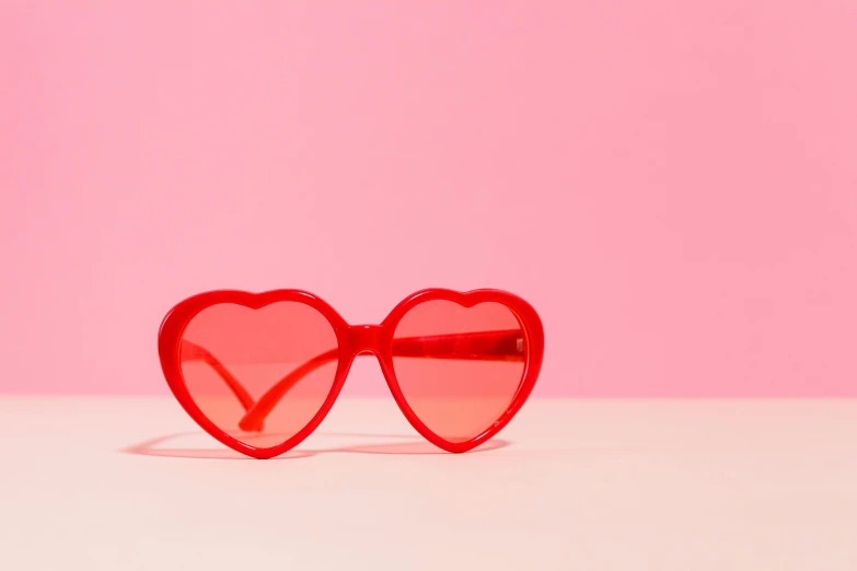 a pair of heart shaped sunglasses on a pink background, an album cover, trending on pexels, wearing red attire, desktop wallpaper, totally radical, overexposed sunlight