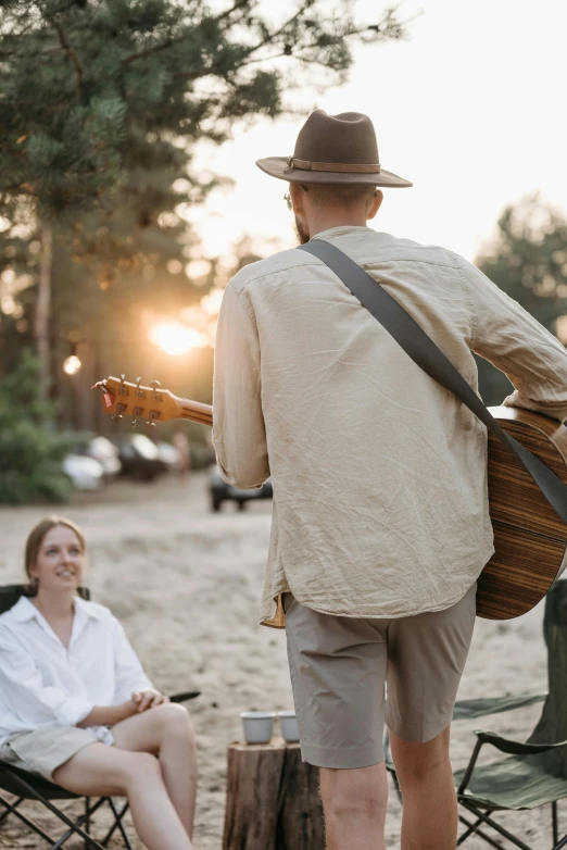 a man playing a guitar next to a woman sitting in lawn chairs, an album cover, by Jan Tengnagel, pexels contest winner, wearing a linen shirt, people enjoying the show, sundown, man standing