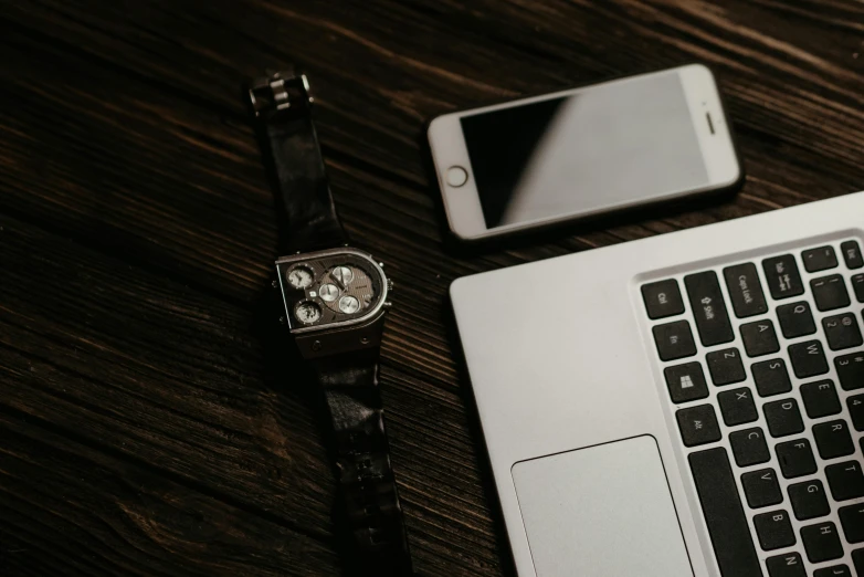 a laptop computer sitting on top of a wooden table, by Romain brook, trending on pexels, wears a watch, phone photo, black and silver, icon