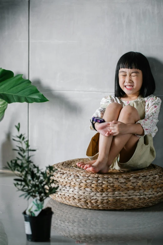 a little girl sitting on top of a wicker basket, inspired by Ni Duan, pexels contest winner, relaxing on a modern couch, natural materials, asian features, standing on a shelf