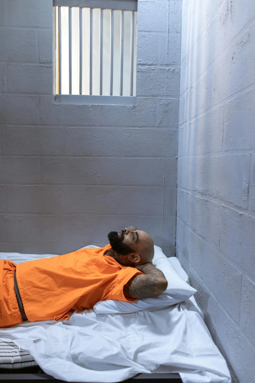 a man laying on a bed in a jail cell, a photo, dressed in orange inmate attire, bald head, 2019 trending photo, vacation photo