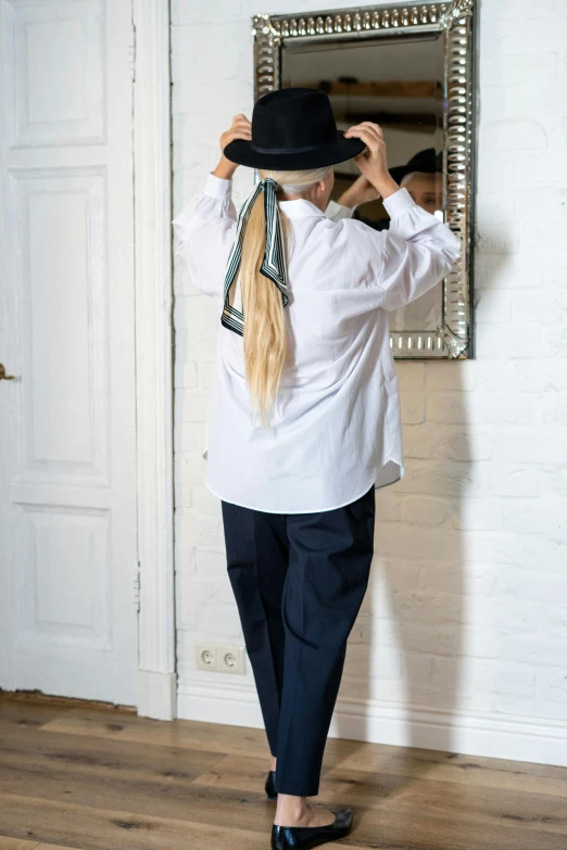 a woman that is standing in front of a mirror, by Nina Hamnett, baggy clothing and hat, navy, fine white shirt, rear-shot