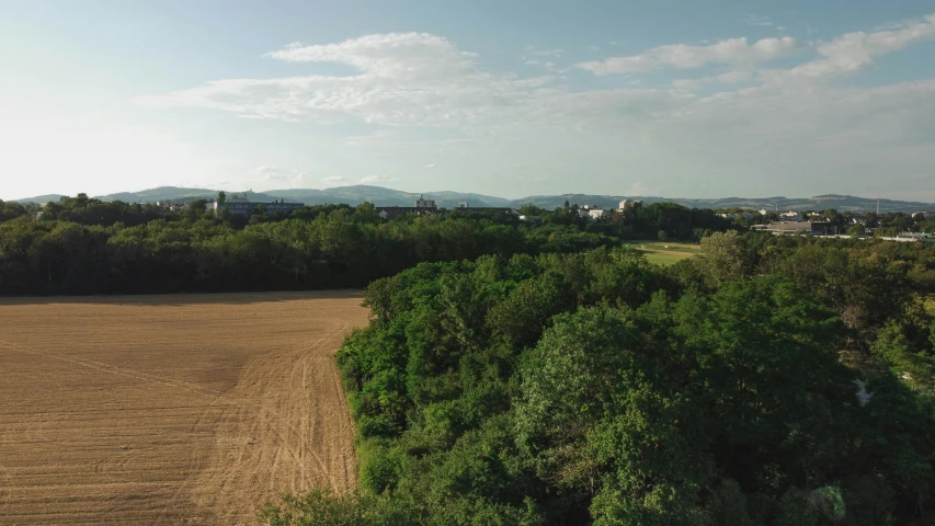 an aerial view of a field with trees in the foreground, inspired by Jan Müller, unsplash, land art, city in the background, low quality footage, nice afternoon lighting, superwide shot