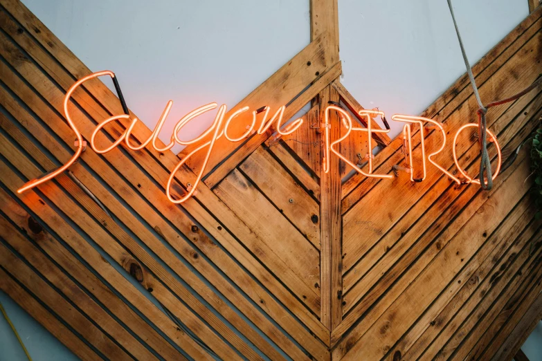 a neon sign sitting on top of a wooden wall, inspired by Lubin Baugin, trending on unsplash, very smoky paris bar, sol retreat, orange neon stripes, wrought iron