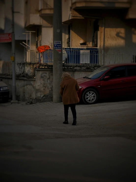 a man walking across a street next to a red car, by Matija Jama, pexels contest winner, realism, bosnian, female image in shadow, 3 am, in a suburb