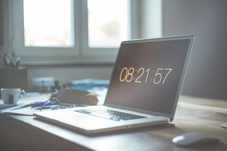 a laptop computer sitting on top of a wooden desk, by Carey Morris, unsplash, clock iconography, evenly lit, written in a neat, taken with sony alpha 9