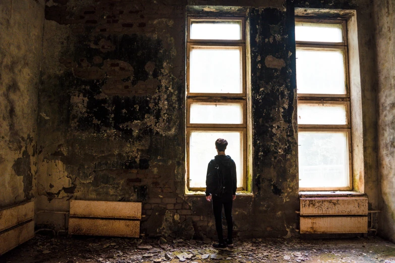 a man standing in front of a window in an old building, pexels contest winner, fan favorite, dystopian grunge, teenage boy, distant full body view