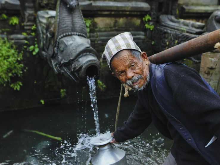 a man that is standing in the water, inspired by Steve McCurry, pexels contest winner, sumatraism, water fountain, old man doing hard work, nepali architecture buildings, anthropology photo”