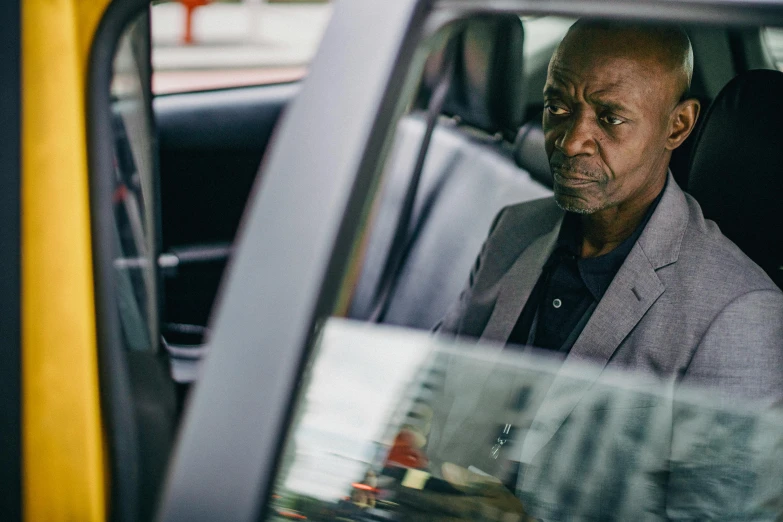 a man sitting in a car looking out the window, by David Begbie, lance reddick, walking down, concerned expression, press shot