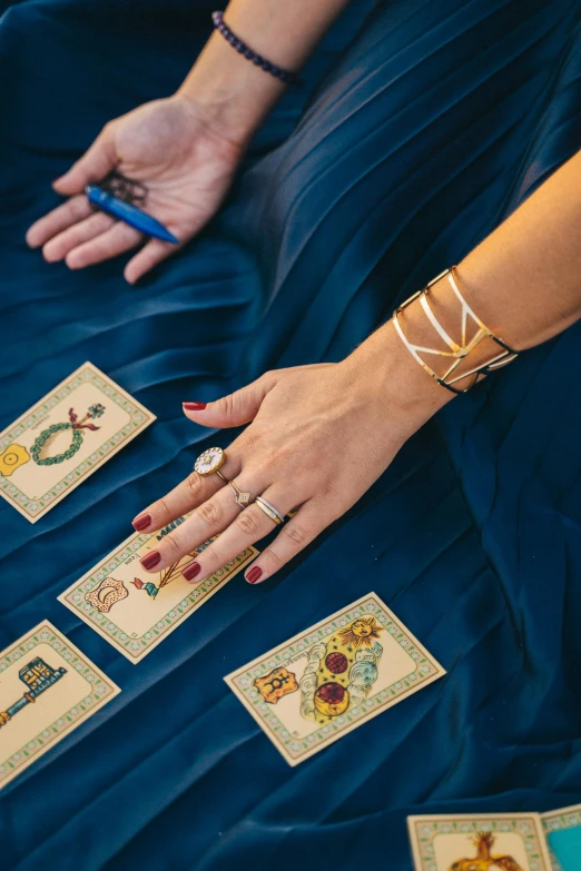 a woman in a blue dress is playing tarot, by Julia Pishtar, bracelets and necklaces, curated collections, chaumet, medium closeup shot