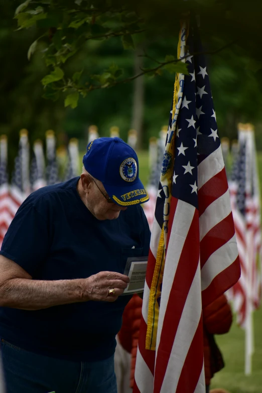 a man standing next to a bunch of american flags, reading, profile image, maintenance photo, during the day