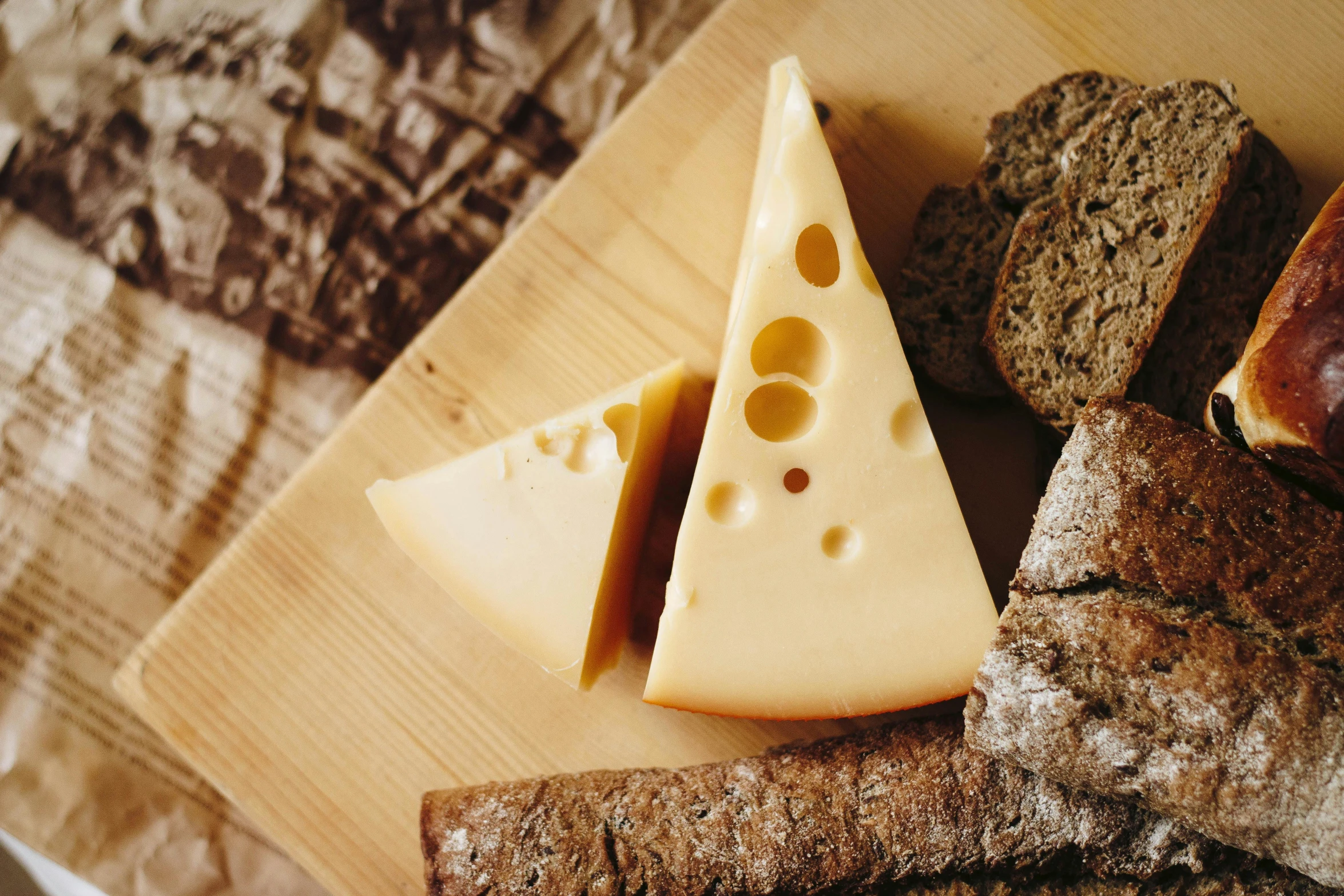 a wooden cutting board topped with bread and cheese, inspired by Géza Dósa, unsplash, made of swiss cheese wheels, thumbnail, mild,