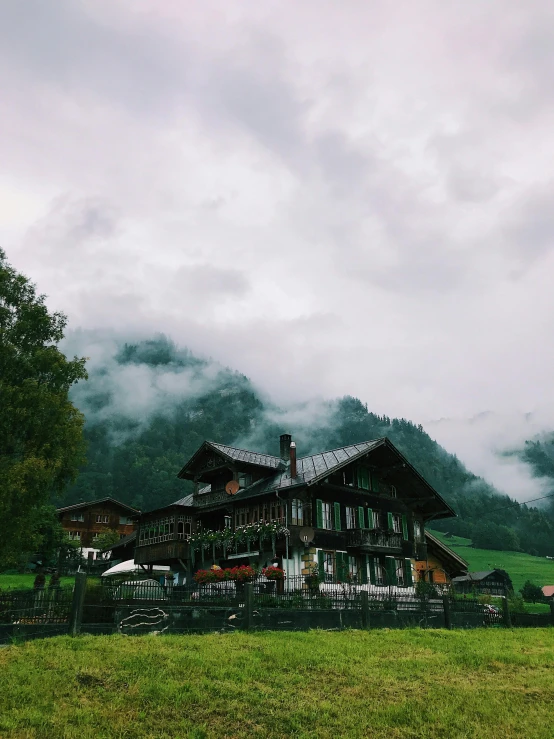 a house sitting on top of a lush green hillside, by Anna Haifisch, pexels contest winner, low clouds after rain, lauterbrunnen valley, ☁🌪🌙👩🏾, snapchat photo