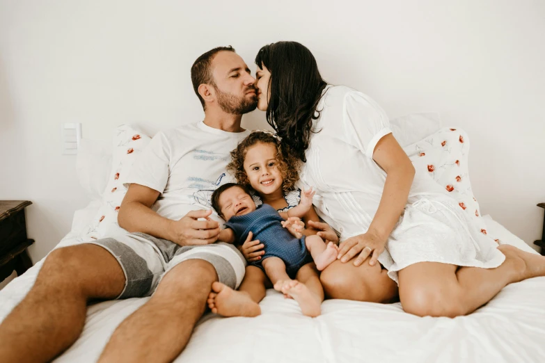 a man and woman sitting on a bed with a baby, kissing each other, lachlan bailey, avatar image, group photo